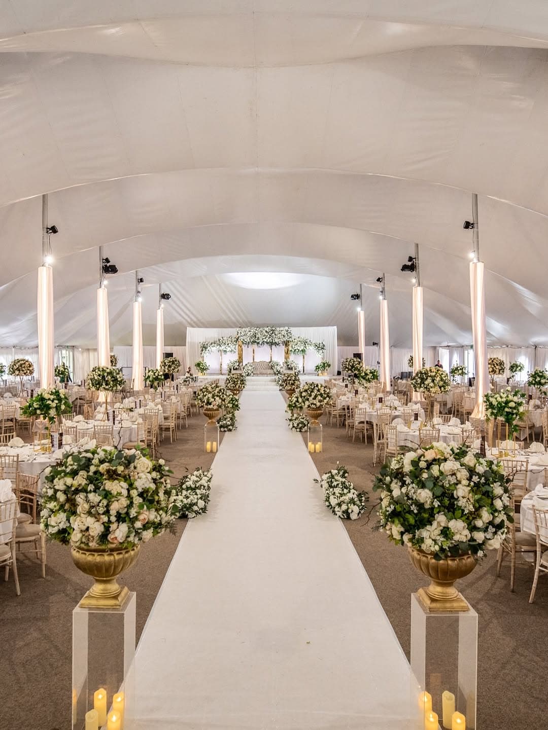 A marquee wedding ceremony aisle leading to a floral arch