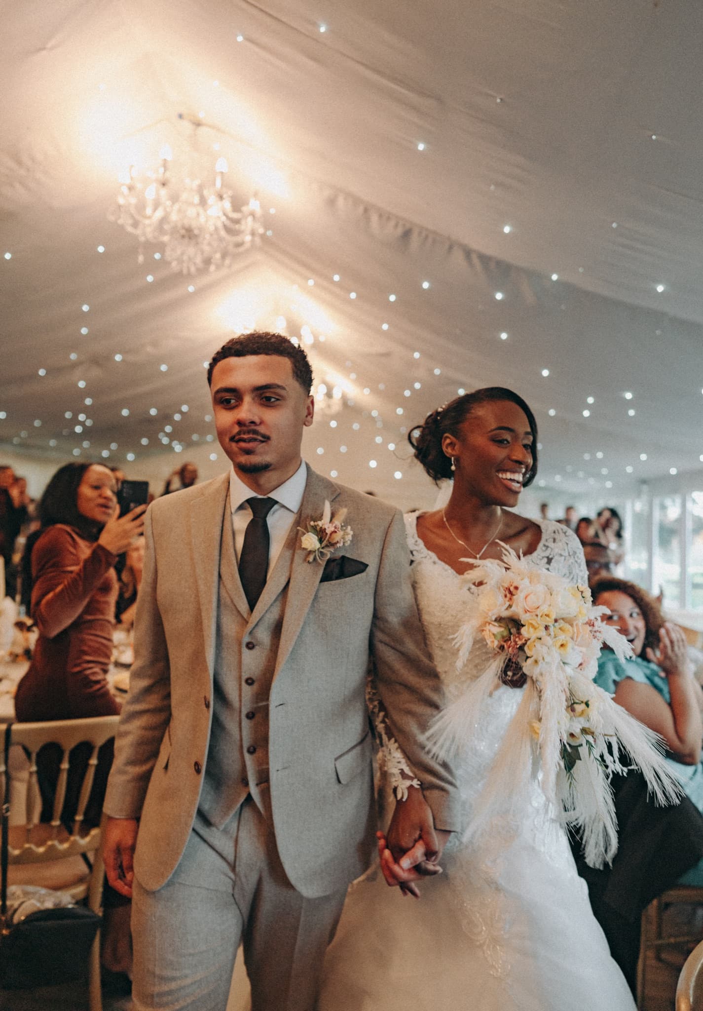 A newly married couple walking through the marquee as their guests celebrate