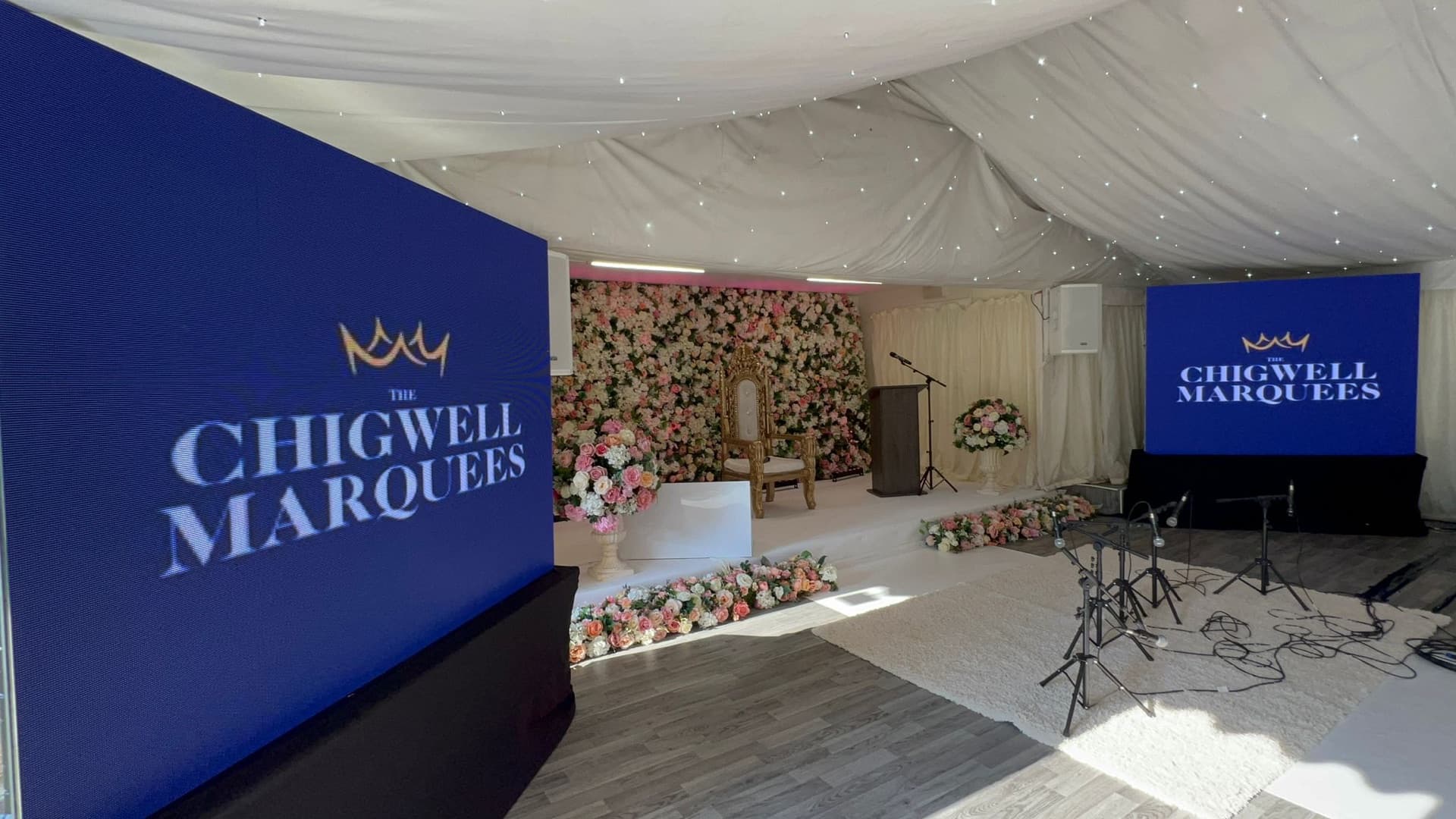 The marquee set for a cultural and religious ceremony with a floral backdrop, gold throne and lectern